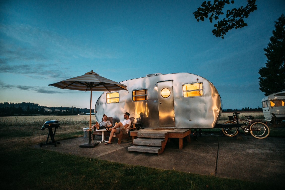couple sitting in front of their mini airstream trailer at evening time